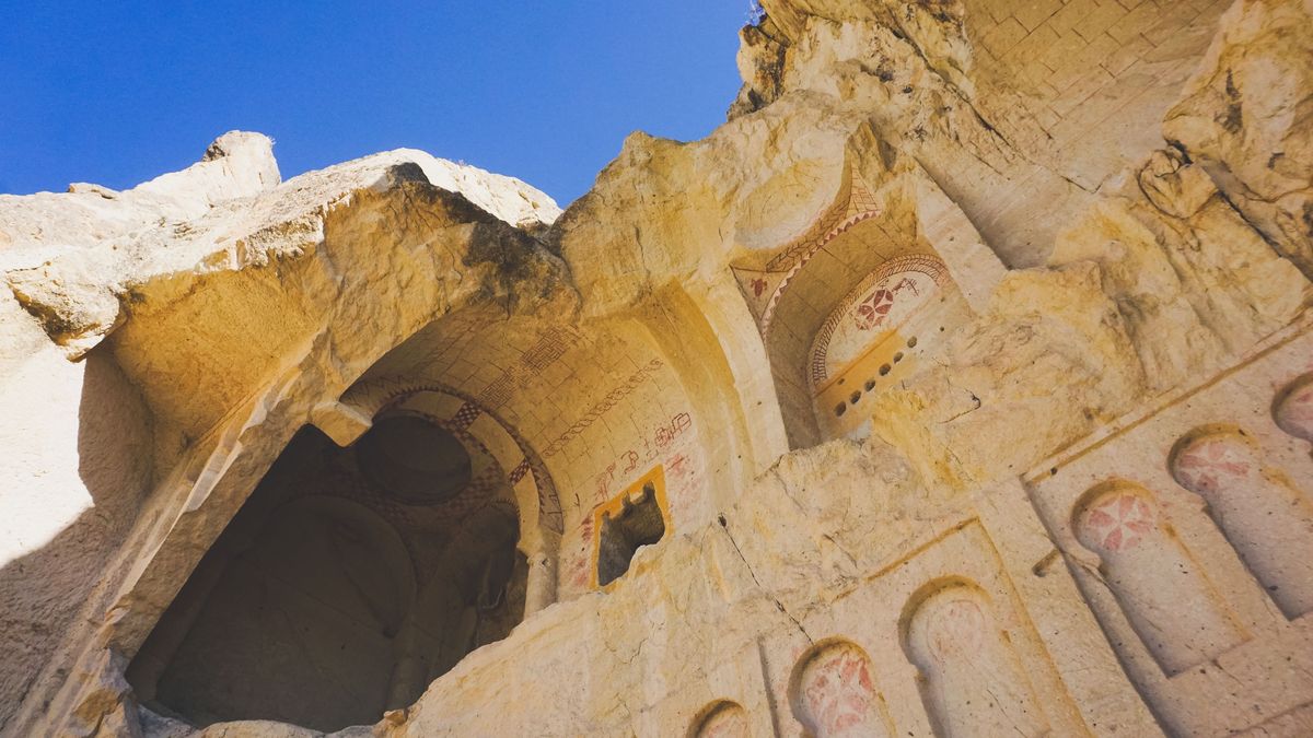 The facade of a rock-cut church in Cappadocia, carved into pale tuff and painted with red-ochre crosses and geometric bands