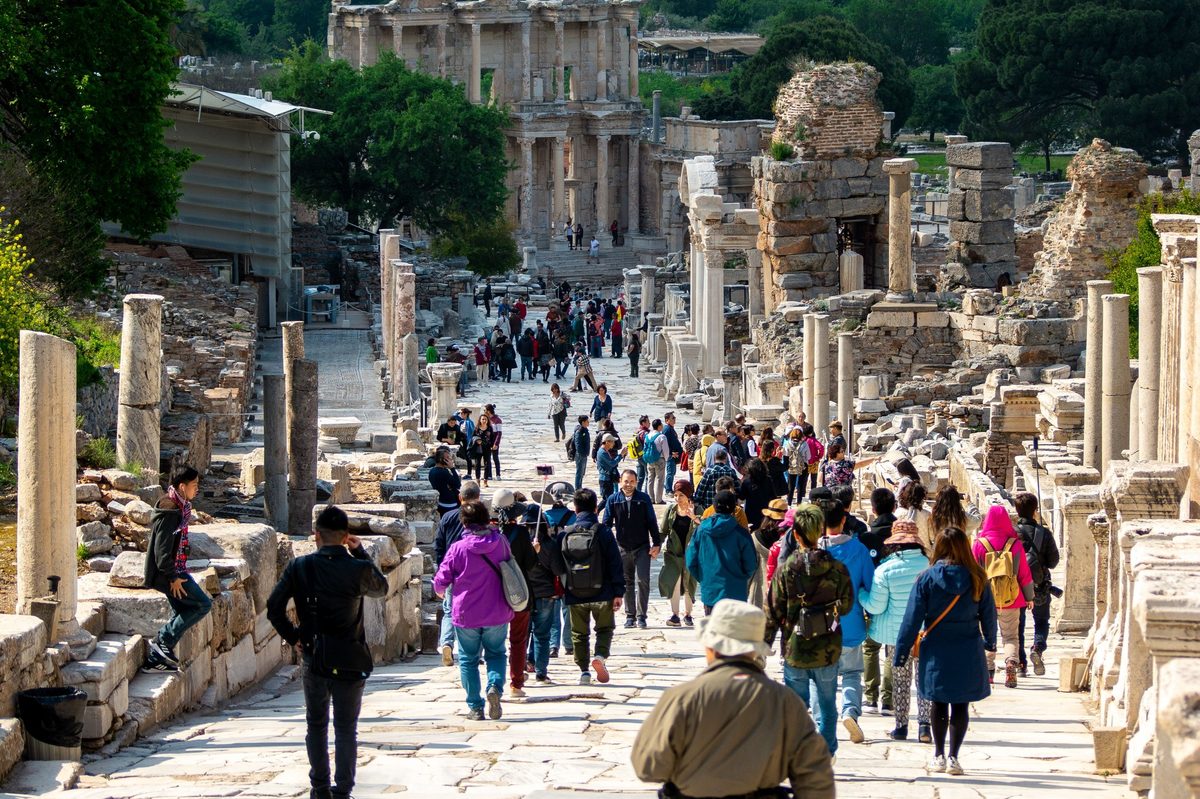 Several tour groups walking down the marble paving of Curetes Street at Ephesus, with the Library of Celsus at the far end